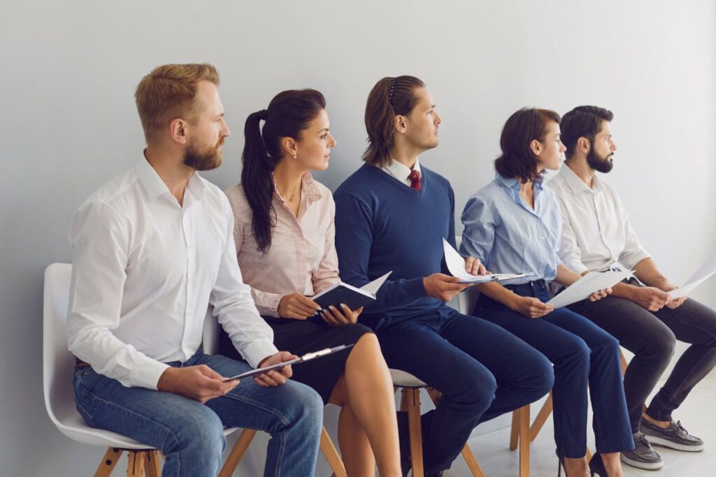 Candidatos aguardando ansiosamente por uma entrevista de emprego, cada um com seus documentos e expectativas.