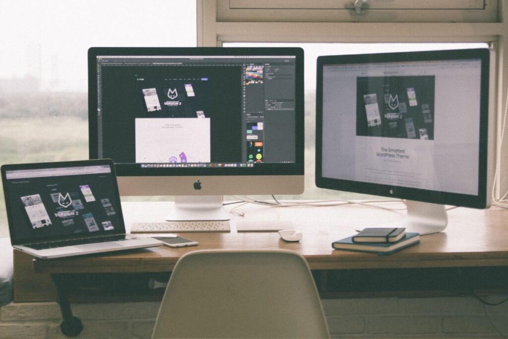 Espaço de trabalho remoto com dois monitores, um laptop e materiais de design.