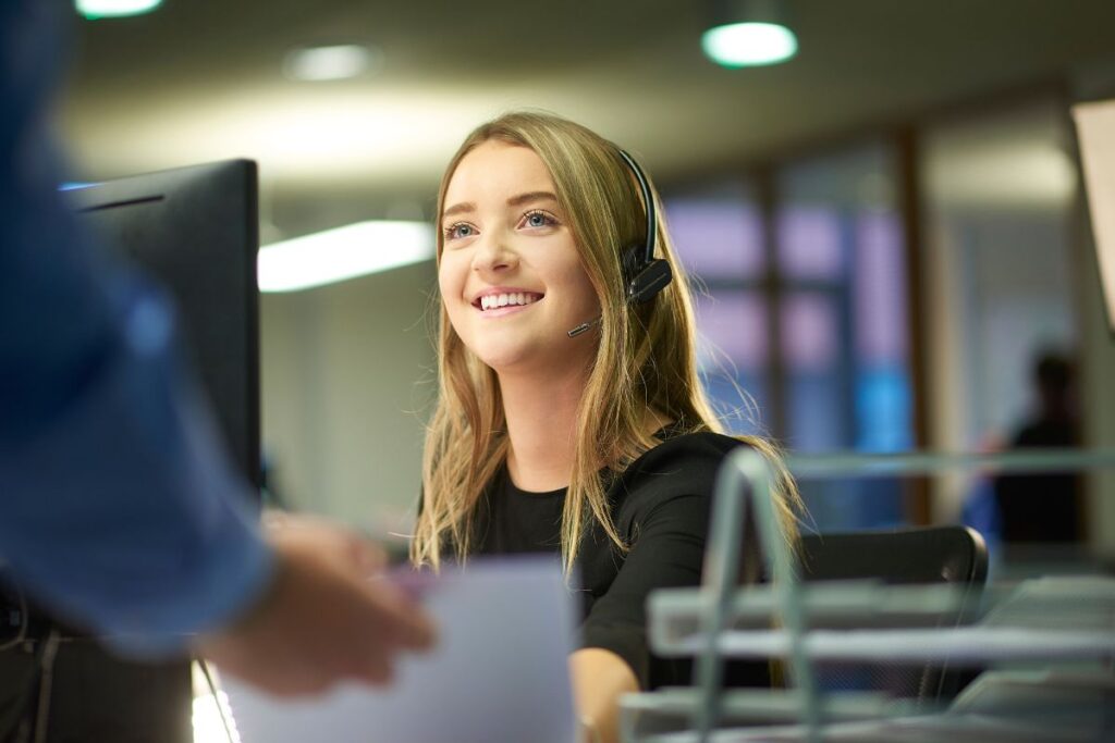Jovem aprendiz com headset sorrindo em um ambiente de escritório, indicando atendimento ou suporte.