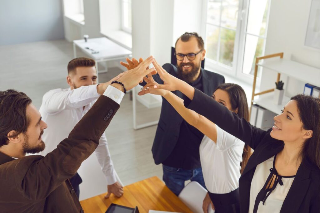 Grupo diverso de profissionais de negócios celebrando com um "high five" em um ambiente de escritório moderno.
