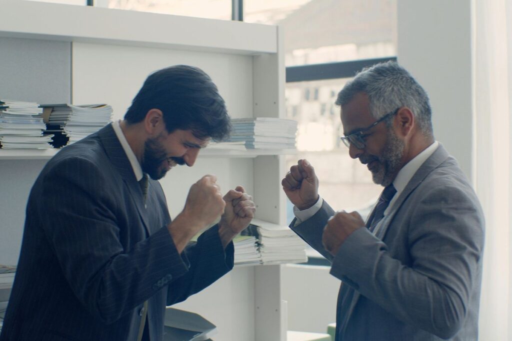 Dois homens de negócios maduros celebrando uma vitória com gestos de sucesso em um escritório.