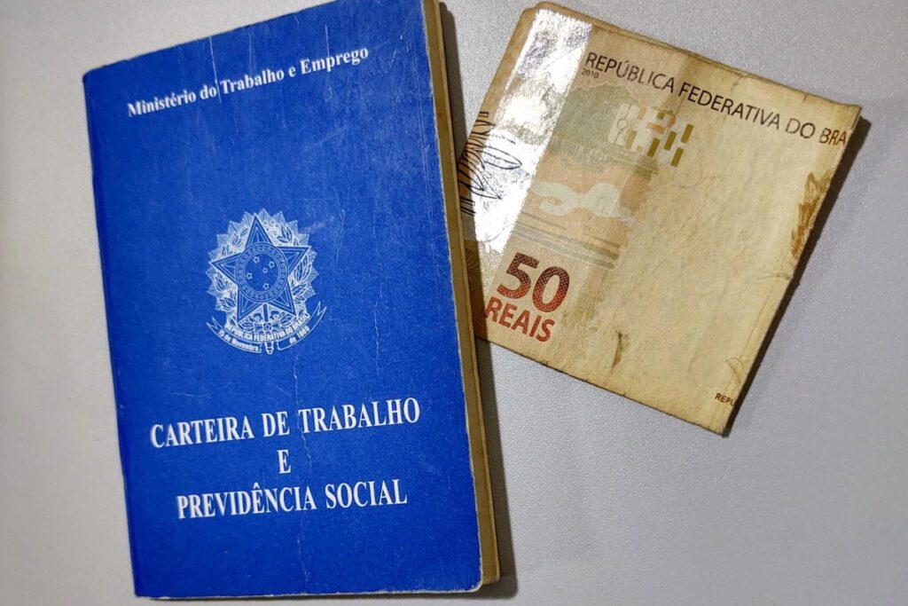 Carteira de Trabalho e Previdência Social ao lado de uma nota de cinquenta reais, simbolizando o 13º salário.