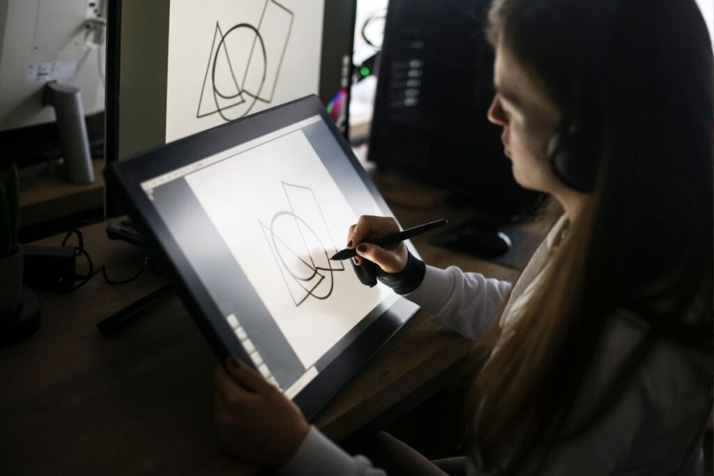 Jovem designer gráfico usando fones de ouvido e um grande monitor interativo com caneta stylus para criar arte digital em seu home office.