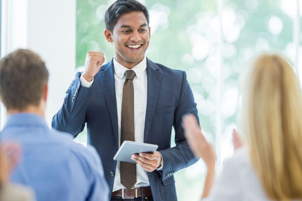 Homem em terno celebrando com entusiasmo em uma apresentação ou reunião.