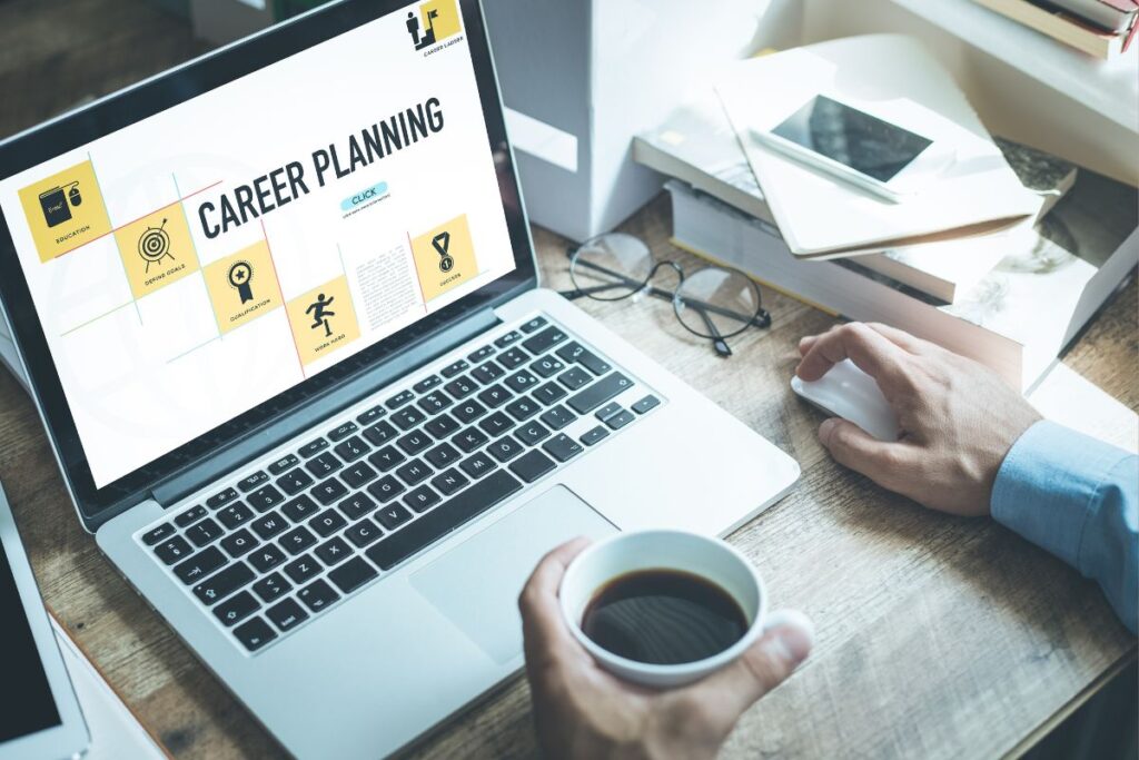 Pessoa sentada à mesa, utilizando um laptop com a tela exibindo "CAREER PLANNING" e ícones representando educação, definição de metas, qualificação, carga de trabalho e sucesso. A pessoa segura uma xícara de café e usa um mouse.