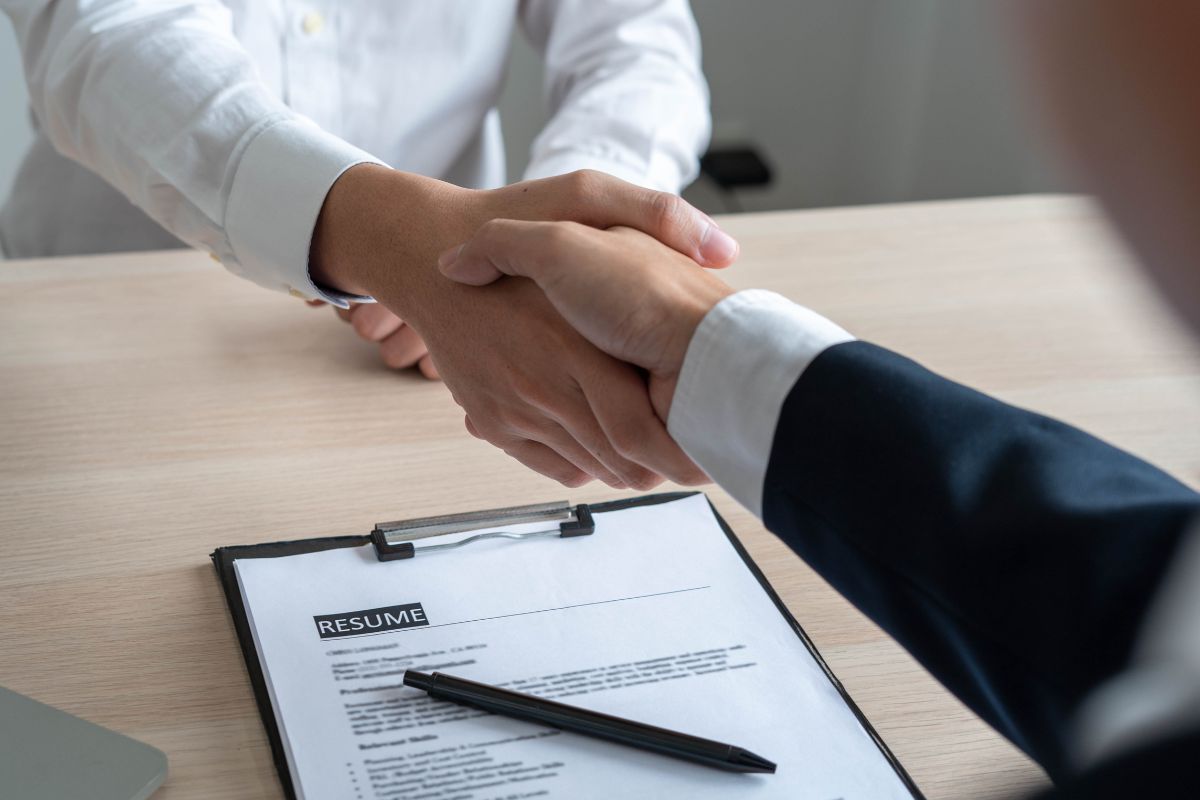 Candidato e recrutador apertando as mãos após entrevista de emprego com currículo profissional sobre a mesa