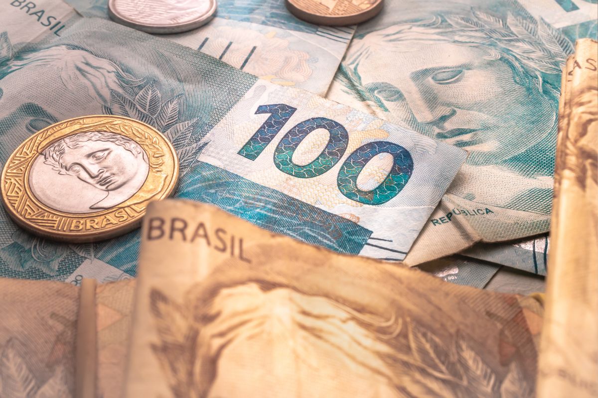 Close-up de notas de cem reais e moedas brasileiras.