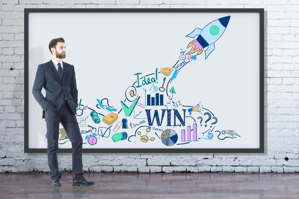 Empresário de terno observando quadro com ilustrações de empreendedorismo, foguete e palavra WIN em parede de tijolos
