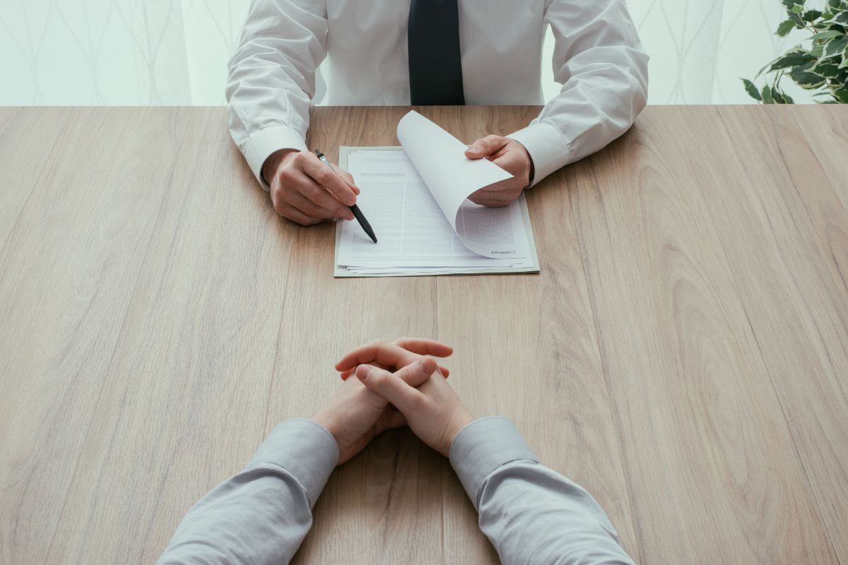 Recrutador revisando um currículo enquanto candidato ouve atentamente durante a entrevista.