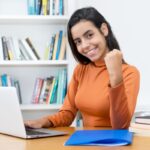 Mulher sorridente comemorando sucesso em frente ao laptop.