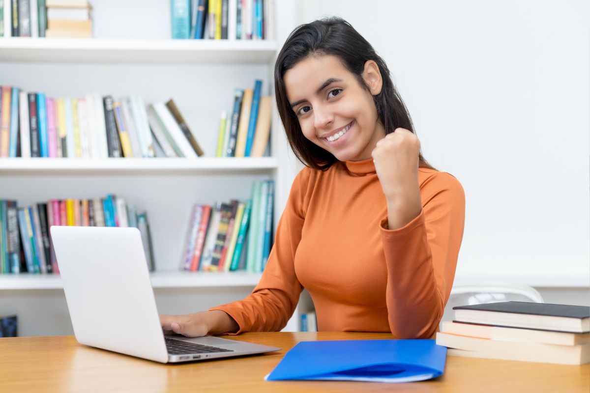 Mulher sorridente comemorando sucesso em frente ao laptop.