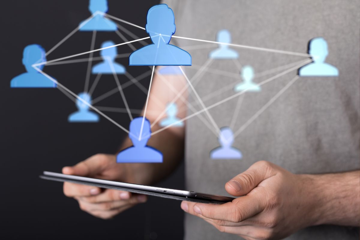 Uma pessoa segurando um tablet, com uma projeção digital de ícones de pessoas azuis conectadas por linhas, ilustrando o uso da tecnologia para networking.