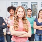 Grupo diversificado e sorridente de jovens profissionais e aprendizes posando com confiança em um ambiente de trabalho moderno.